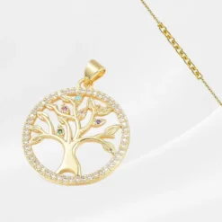 Pendentif Arbre de Vie en acier inoxydable plaqué or, médaillon rond ajouré avec un arbre stylisé aux branches ornées de zircons multicolores (turquoise, rose, mauve, vert) et un contour serti de zircons blancs, suspendu à une fine chaîne dorée forçat, photographié sur fond blanc satiné.