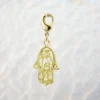 Charm Main de Fatma ciselée en métal doré plaqué or 1 micron, avec mousqueton, motifs ajourés et cœur central, fond blanc, 25x23 mm