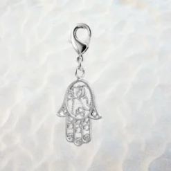 Charm main de Fatma argenté en métal argenté, motif ajouré filigrane avec cœur gravé et zirconiums, fermoir mousqueton pour bracelet à charms — fond sable clair