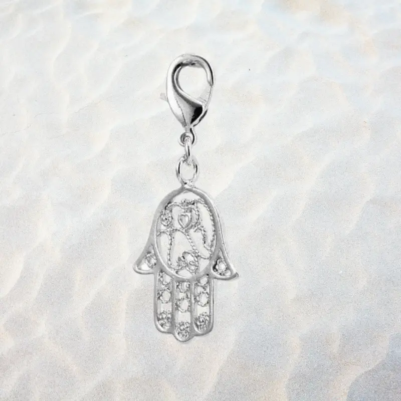 Charm Main de Fatma 2 Charm main de Fatma argenté en métal argenté, motif ajouré filigrane avec cœur gravé et zirconiums, fermoir mousqueton pour bracelet à charms — fond sable clair