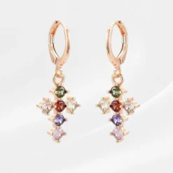 Boucle d'oreille Croix 9 Paire de boucles d'oreilles créoles or rose, pendentif croix sertie de zircons multicolores – vert, rouge, blanc, violet et rose – bijou croix femme coloré tendance sur fond satiné blanc