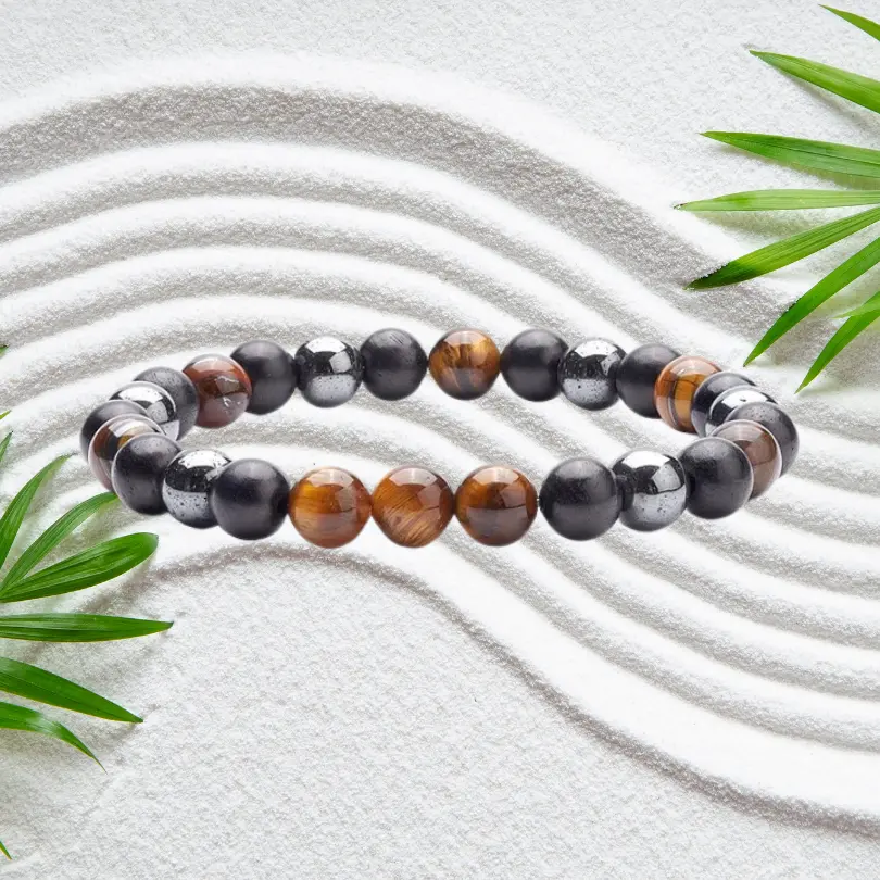 Bracelet Hématite 1 Bracelet hématite en pierres naturelles noires et œil de tigre brun doré, perles rondes de 8 mm montées sur élastique, posé sur sable blanc zen avec feuilles de bambou — bijou unisexe homme femme