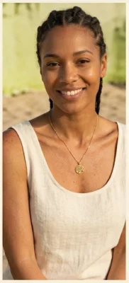 Quels bijoux porter selon les saisons ? 3 Femme portant un collier doré avec pendentif rond ajouré, sur un haut clair sans manches, dans une lumière naturelle douce
