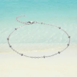 Chaîne de Cheville Perle 15 Chaîne de cheville argentée en acier inoxydable maille forçat avec mini perles argentées intercalées, rallonge fine, fermoir mousqueton, fond plage sable blanc