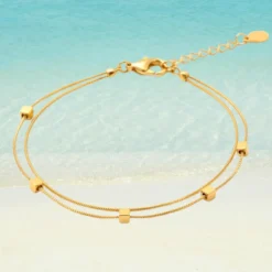 Chaîne de Cheville Perle 13 Chaîne de cheville dorée double rang en acier inoxydable avec perles carrées dorées, maille serpent fine, fermoir mousqueton et rallonge à goutte, fond plage turquoise