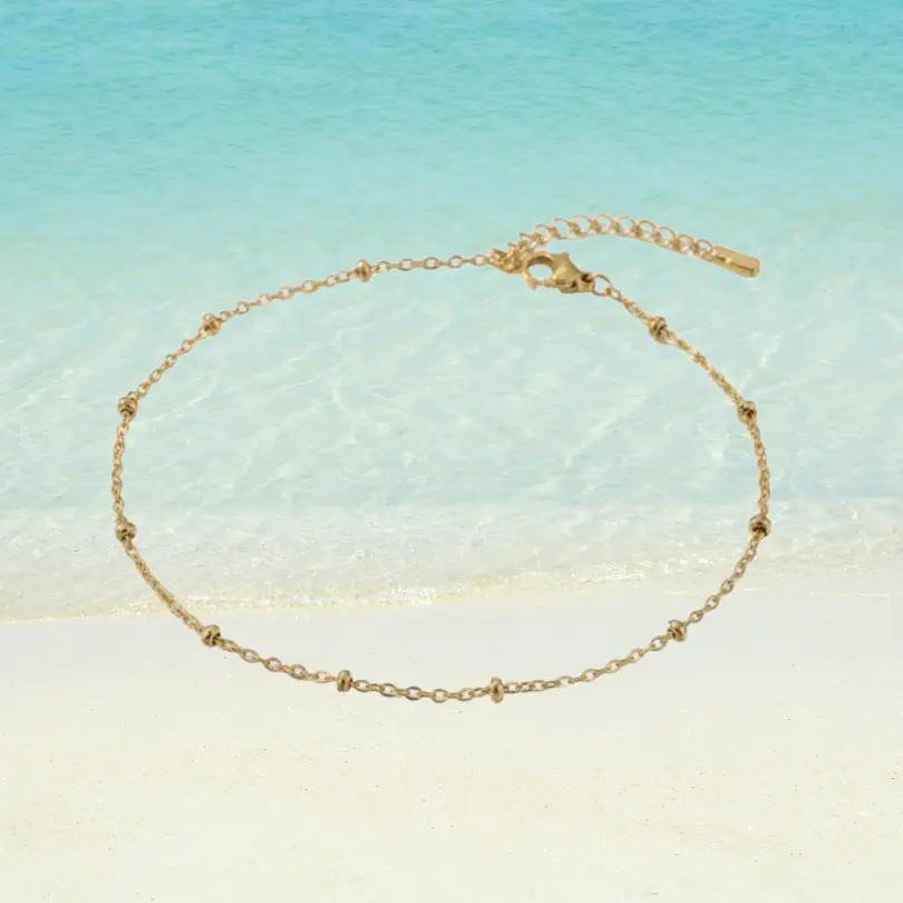 Chaîne de Cheville Perle 7 Chaîne de cheville dorée en acier inoxydable maille forçat avec mini perles dorées intercalées, rallonge barrette, fermoir mousqueton, fond plage turquoise