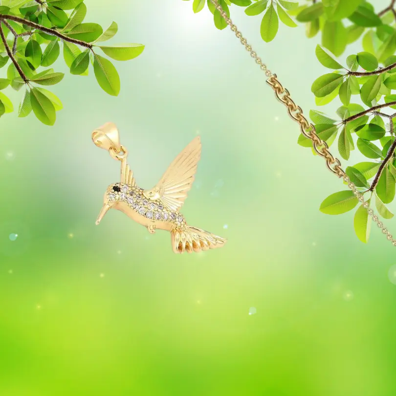 Pendentif Oiseau 4 Pendentif oiseau entièrement doré à l'or fin, serti de zirconiums blancs transparents pavés sur le corps du colibri , ailes texturées dorées — collier bijou femme sur fond vert naturel, chaîne dorée visible