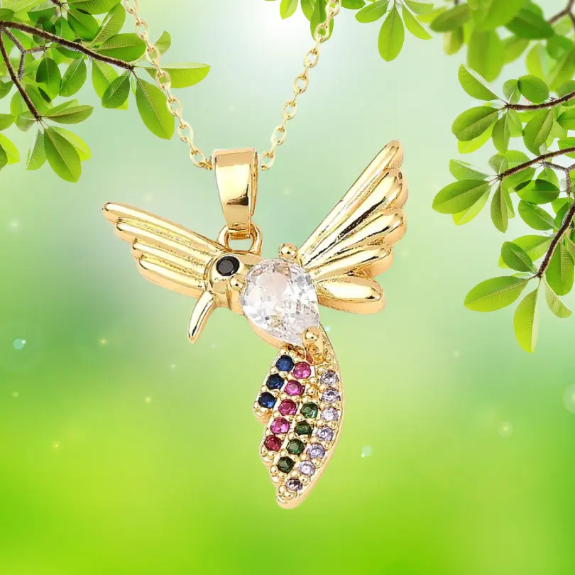 Pendentif Oiseau 2 Pendentif oiseau doré à l'or fin avec zirconiums multicolores (rose, bleu, vert, violet, noir) pavés sur le corps du colibri — collier bijou femme suspendu sur fond naturel vert, chaîne dorée visible