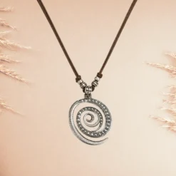 Accueil 15 Collier Bohème pendentif spirale en métal argenté vieilli sur cordon cuir marron ajustable, photographié sur fond beige rosé avec épis de pampa — bijou fantaisie ethnique femme